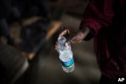 FILE - An African migrant fills an empty bottle with leaking water from the roof of a barrack in a detention center for illegal migrants in Abu Salim district on the outskirts of Tripoli, LIbya, Nov. 29, 2013.