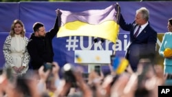 Predsjednik Ukrajine Volodymyr Zelenskyy, drugi lijevo, i predsjednik Litvanije Gitanas Nauseda, drugi desno, drže ukrajinsku zastavu dok se obraćaju okupljenima tokom događaja na marginama samita NATO-a u Vilniusu, Litvanija, u utorak, 11. jula 2023.