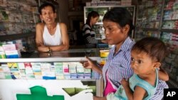 In this Aug. 26, 2009 file photo, a merchant speaks with a woman holding her ill child at a pharmacy in Pailin, Cambodia.