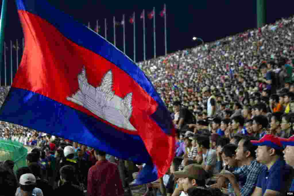 អ្នកគាំទ្រកាន់ទង់ជាតិប្រទេសកម្ពុជា ដើម្បីលើកទឹកចិត្តក្រុមបាល់ទាត់ជម្រើសជាតិកម្ពុជា ក្នុងការប្រកួតជាមួយក្រុមសឹង្ហបុរី ក្នុងការប្រកួតជំរុះវគ្គបឋមអាស៊ី ដើម្បីឈានទៅកាន់ការប្រកួតពានរង្វាន់ពិភពលោក នៅពហុកីឡាដ្ឋានជាតិអូឡាំពិក កាលពីថ្ងៃទី១១ ខែមិថុនា ឆ្នាំ២០១៥។