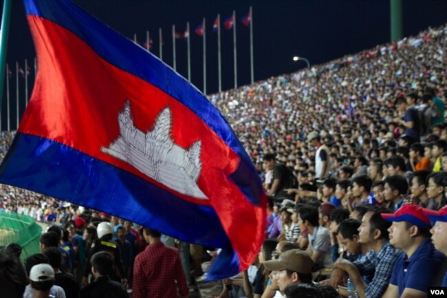 អ្នកគាំទ្រកាន់ទង់ជាតិប្រទេសកម្ពុជា ដើម្បីលើកទឹកចិត្តក្រុមបាល់ទាត់ជម្រើសជាតិកម្ពុជា ក្នុងការប្រកួតជាមួយក្រុមសឹង្ហបុរី ក្នុងការប្រកួតជំរុះវគ្គបឋមអាស៊ី (នូវ ពៅលក្ខិណា/VOA)