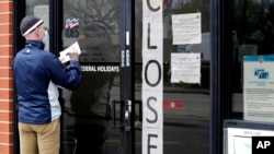 FILE - In this April 30, 2020 file photo, a man writes information in front of Illinois Department of Employment Security in Chicago. 