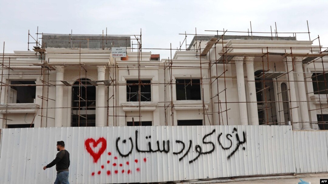 A man walks past graffiti reading in Kurdish "Long live Kurdistan,” near the scene of a rocket attack in Irbil, the capital of the northern Iraqi Kurdish autonomous region, Feb. 16, 2021. 