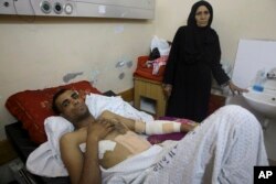Marwan Shtewi, 32, lies in bed while his mother, Fatma, stands near him in Shifa hospital in Gaza City, May 16, 2018. Shtewi didn't tell his mother or his fiancee he was going to the protest. "I would have barred him," his mother said.