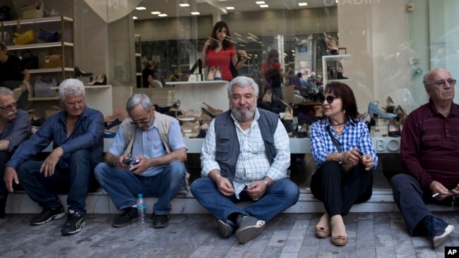 希腊退休人员坐在雅典一家鞋店前等候参加集会，抗议政府的国际债务救助计划的改革。（2018年4月25日）