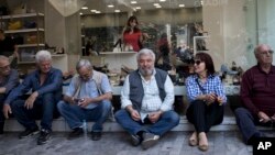 Pensioners sit outside a shoe shop as they take part in a rally near the Finance Ministry in central Athens, April 25, 2018. Thousands of people have taken to the streets of Athens to protest against a number of bailout-related reforms, including the sale of some power plants, potential pension cuts and staffing funding cuts for state-run hospitals.