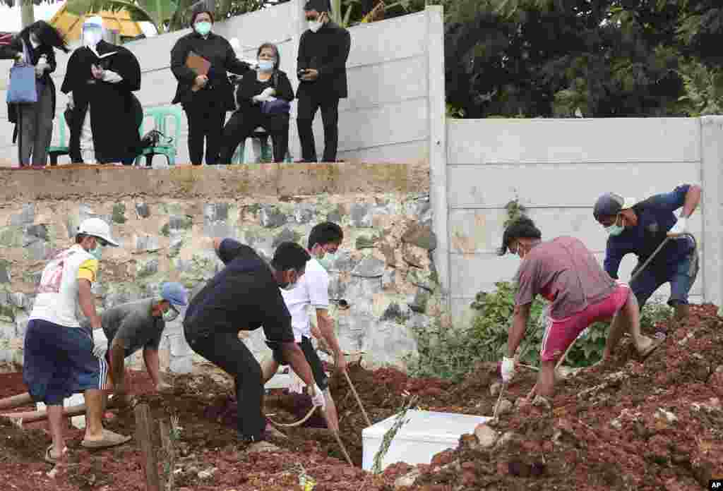 Para pekerja menguburkan jenazah seorang pria yang meninggal akibat Covid-19, sementara anggota keluarganya menyaksikan di pemakaman Jombang, yang disediakan khusus untuk menampung lonjakan kematian akibat pandemi virus corona di Tangerang, Selasa, 26 Januari 2021. (Foto AP / Tatan Syuflana)
