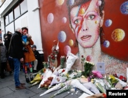 A woman wearing Ziggy Stardust style makeup weeps as she visits a mural of David Bowie in Brixton, south London, Jan. 11, 2016.