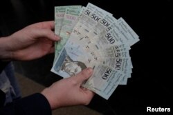 A man holds 500 and 5000 bolivar banknotes for a photo in Caracas, Venezuela, Jan.16, 2017.