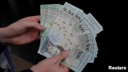 FILE - A man holds 500 and 5000 bolivar banknotes for a photo in Caracas, Venezuela, Jan.16, 2017. 