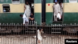 FILE - A man passes through a railing while others board a train as they make their way home at the Cantonment railway station in Karachi, Pakistan, July 5, 2016. 