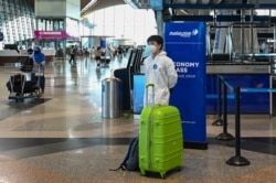 Seorang penumpang yang mengenakan alat pelindung diri (APD), berdiri di dekat barang bawaannya di Bandara Internasional Kuala Lumpur (KLIA), Sepang, 29 November 2021.