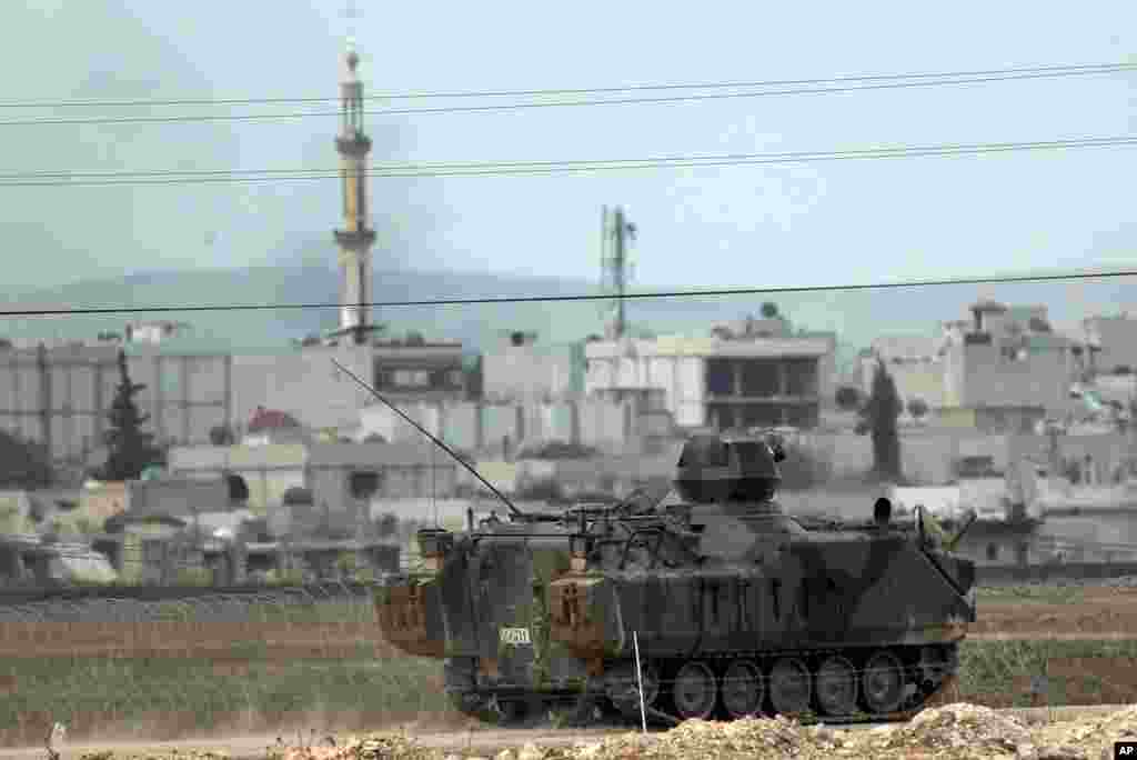 Backdropped by Kobani, in Syria, a Turkish forces armored vehicle patrols the border road in Mursitpinar, on the outskirts of Suruc, on the Turkey-Syria border, Oct. 14, 2014.