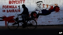 A man rides his bicycle past graffiti on a wall urging a boycott of the April 21 Formula One Bahrain Grand Prix with an image of Crown Prince Salman Al Khalifa in a racing car in Bar Bar, Bahrain, April 8, 2013.