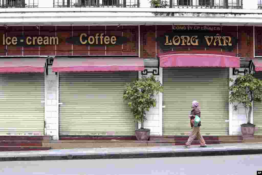 یک زن از کنار مغازه&zwnj;ها و کافه&zwnj;های بسته در هانوی ویتنام می&zwnj;گذرد.