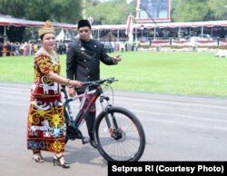Istri Wakil Ketua MPR – Agati Sulie Mahyudin – yang mengenakan pakaian adat Dayak nampak menggandeng sepeda hadiah dari Presiden Joko Widodo (Courtesy: Setpres RI)