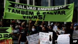 Demonstrators hold Portuguese messages like "Saving jobs is also saving lives" outside a city government office to protest a two-week-long lockdown to curb the spread of COVID-19 in Brasilia, Brazil, March 1, 2021.