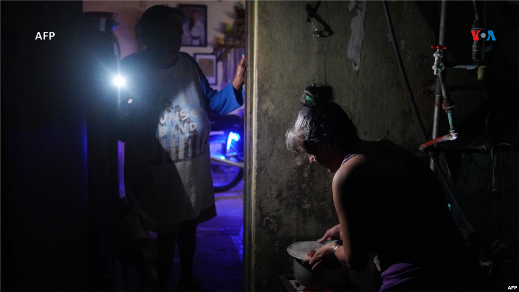 Una mujer hierve agua mientras otra enciende la luz de un teléfono móvil durante un apagón nacional provocado por una falla de red en Matanzas, Cuba.