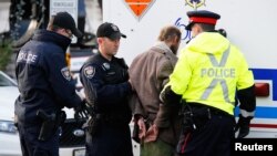 FILE- Police officers search a man arrested after approaching police tape near the Canada War Memorial while Prime Minister Stephen Harper paid respect to Cpl. Nathan Cirillo at the memorial in Ottawa, Oct. 23, 2014. 