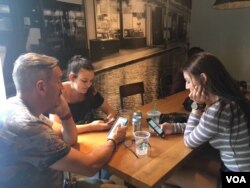 Family at a local Starbucks consult their smartphones in a Starbucks in Washington D.C. (VOA/CMaddux)