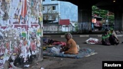 People sit next to torn election posters at a street in Dematagoda, Colombo, Sri Lanka, September 7, 2024. 