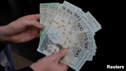 FILE - A man holds 500 and 5,000 bolivar banknotes for a photo in Caracas, Venezuela, Jan.16, 2017. 