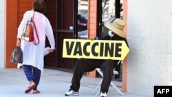 Arhiva - Čovjek sa maskom sjedeći drži putokaz "Vakcina" ispred mobilne klinike za vakcinaciju, u Krenšou bulevaru u Los Anđelesu, Kalifornija, 16. jula 2021.
