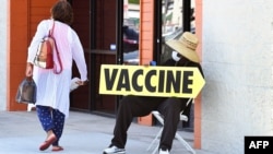A seated man wearing a face mask holds a sign pointing to a mobile vaccination clinic on July 16, 2021, along Crenshaw Boulevard in Los Angeles, California. - Covid cases across America are rising in all 50 states as the Delta variant spreads with…