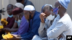 Men from West Africa sit near the site where five people were found dead after a house fire in suburban Denver, Aug. 5, 2020. 