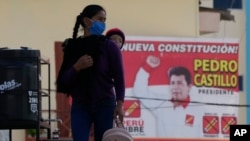 A woman carries her child on her back past an electoral poster promoting Free Peru party presidential candidate Pedro Castillo in his hometown of Tacabamba, Peru, June 5, 2021. 