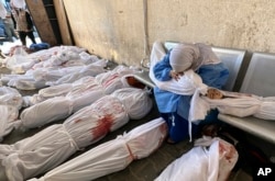 FILE - A Palestinian woman holds the body of a child as she sits by bodies of Palestinians killed by Israeli airstrikes on Jabaliya refugee camp, at the Indonesian hospital, northern Gaza Strip, Nov. 18, 2023.