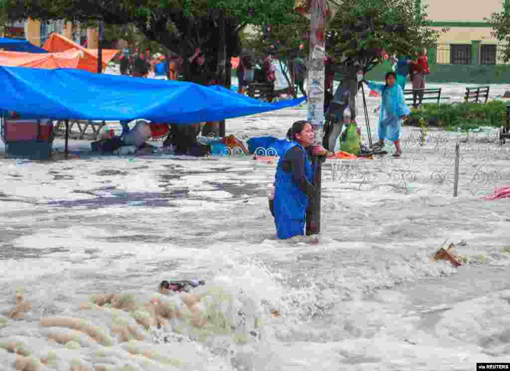 A woman clings to a lamp post during flooding caused by heavy rains in Sucre, Bolivia, Jan. 4, 2021. (Credit: Correo del Sur/Carlos Rodriguez)