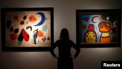 An employee at Christie's poses with Joan Miro's "L'Oiseau au plumage deploye vole vers l'arbre argente" (R) and "Painting (Women, Moon, Birds)" in London, Jan. 8, 2015.