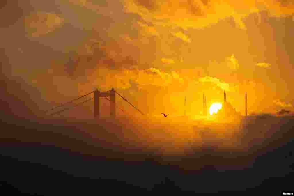 The sun rises behind the Grand Camlica Mosque as July 15 Martyrs&#39; Bridge, known as the Bosphorus Bridge, and the Bosphorus are covered in fog in Istanbul, Turkey.