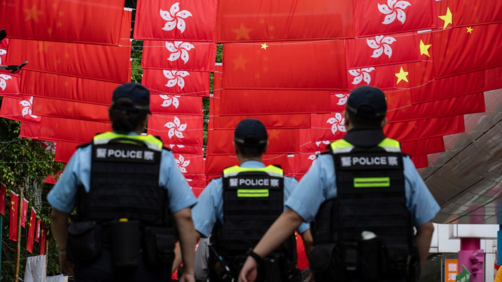 FILE - Police walk past Chinese and Hong Kong flags in Hong Kong, July 1, 2024. As economic pressures constrain budgets, Chinese police have been using flexible legal codes and financial punishments to fill government coffers, analysts say.