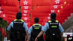 FILE - Police walk past Chinese and Hong Kong flags in Hong Kong, July 1, 2024. As economic pressures constrain budgets, Chinese police have been using flexible legal codes and financial punishments to fill government coffers, analysts say.