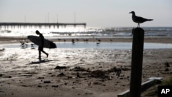 A surfer walks along the beach in Port Aransas, Texas, Sept. 30, 2017. 