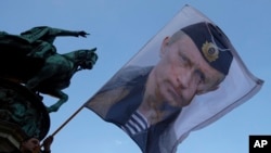 FILE - A man waves a flag showing Russian President Vladimir Putin in front of the monument of late Serbian Duke Mihailo Obrenovic in Belgrade, Serbia, Sept. 24, 2016.