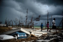 FILE - People walk next to a shattered and water-filled coffin that lies exposed to the elements in the aftermath of Hurricane Dorian, at the cemetery in Mclean's Town, Grand Bahama, Bahamas, Sept. 13, 2019.