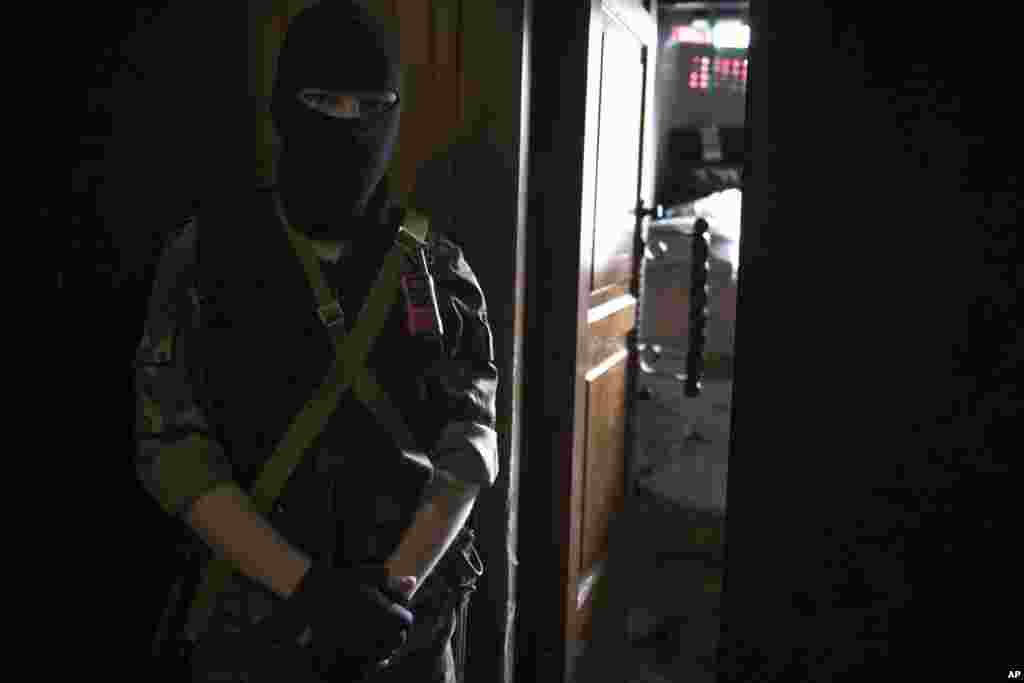 A masked pro-Russia insurgent guards an entrance to the Ukrainian regional office of the Security Service. A Russian national flag is in the background, Luhansk, April 21, 2014.