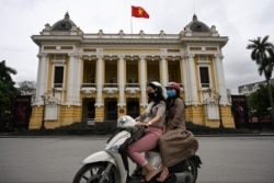Women wearing face masks ride past the Opera House in Hanoi on April 23, 2020, as Vietnam eased its nationwide social isolation efforts.