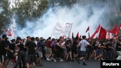 Demonstrators run away from tear gas as they clash with riot police during a demonstration against government plans to regulate street protests, in front of the parliament building in Athens, Greece, July 9, 2020. 