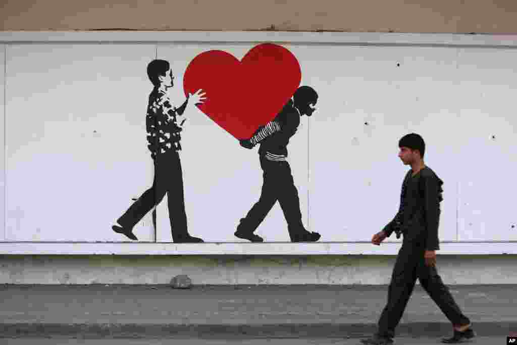 An Afghan boy walks in front of street art on a barrier wall of the NDS (National Directorate of Security) in Kabul.