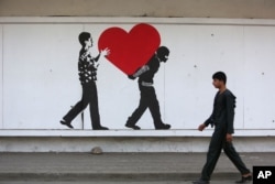 An Afghan boy walks in front of street art on a barrier wall of the National Directorate of Security in Kabul, Aug. 20, 2015.