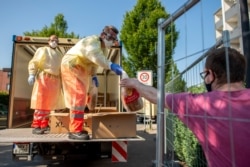 Red Cross staffers wearing face masks and protective clothing distribute bread to residents of a house that has been quarantined, in Verl, Germany, June 21, 2020.