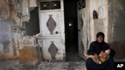Женщина с ребенком на руках сидит у своего разрушенного обстрелом дома в сирийском городе Тремсе. 14 июля 2012 г.