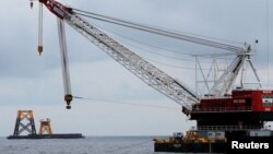 FILE - A construction crane floats next to a barge carrying jacket support structures and a platform for a turbine for a wind farm off Block Island, Rhode Island, July 27, 2015.