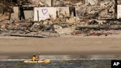 A kayaker goes past a row of homes damaged by the Palisades Fire, Jan. 15, 2025, in Malibu, Calif. 