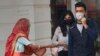 An elderly Indian woman seeks alms as youth wearing pollution masks walk through a shopping area in New Delhi, India, Nov. 14, 2019.