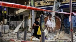 Bir kadın Gazze Şeridi'nden fırlatılan bir roketin Tel Aviv'e düştüğü yerin önünden geçiyor- 7 Ekim 2023